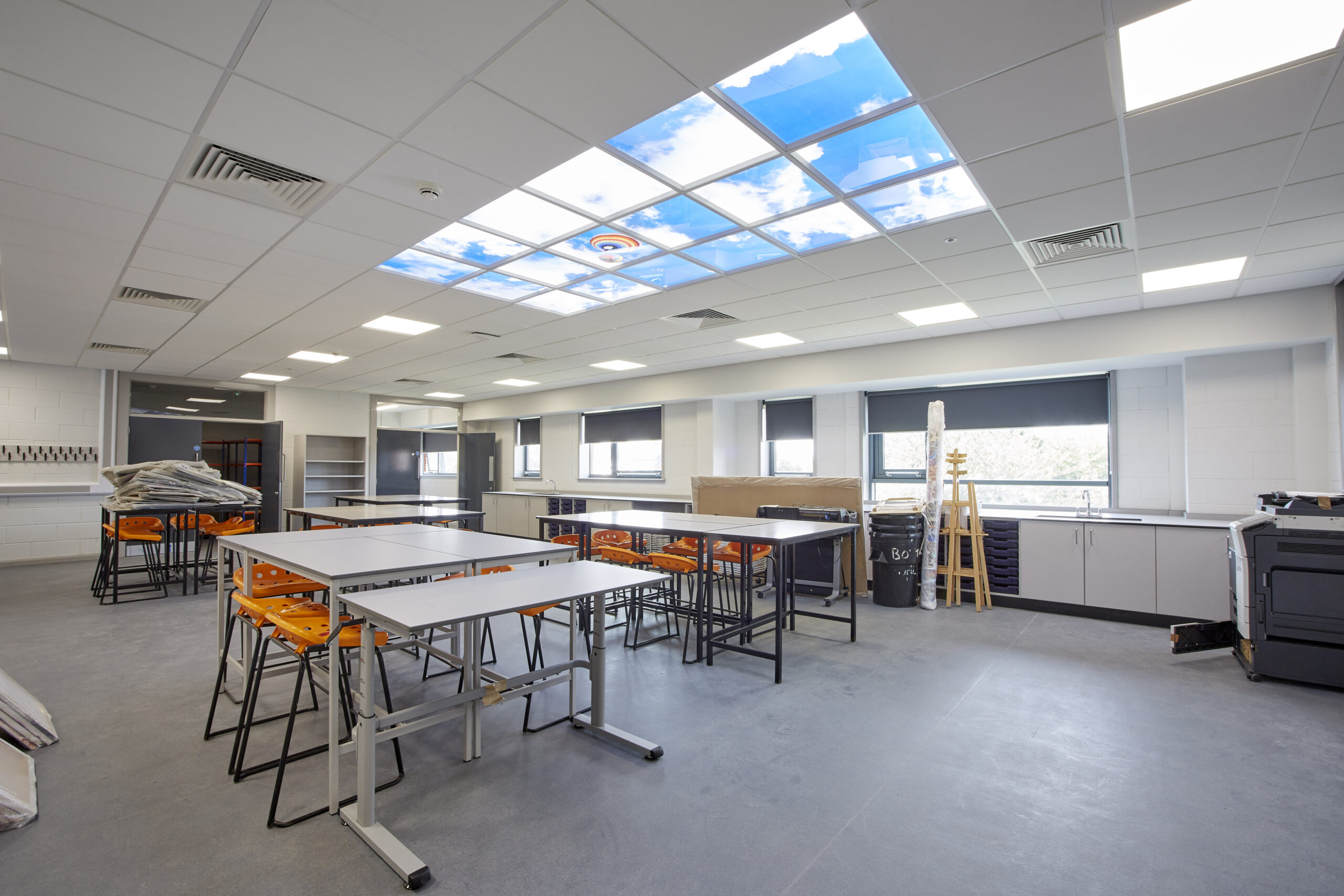 An interior shot of a refurbished art room at Hull Trinity House Academy, with a ceiling light showing blue sky, and art tables set up ready for a class to arrive.